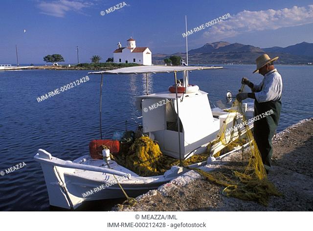 Fisherman cleaning fishing net and view of Agios Spyridon church  Elafonissos, Peloponnese, Greece