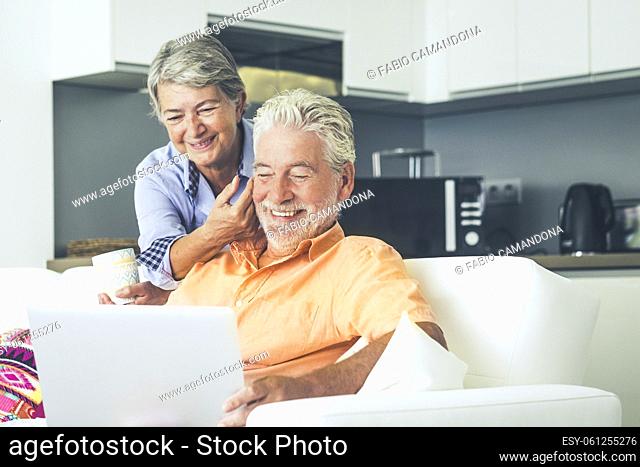Elderly real lifestyle people using computer at home. Leisure indoor activity with man and woman enjoying laptop and internet connection sitting on the sofa...