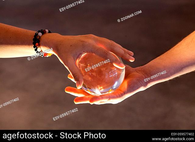 Two young hands holding each a side of a crystal ball. The girls wears bracelets. Closeup shot