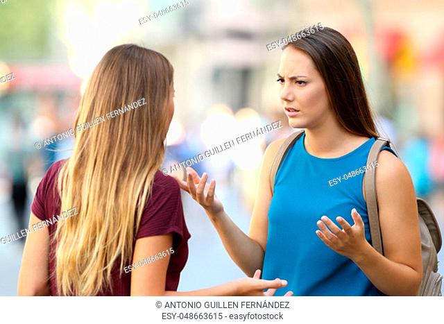Two angry women friends talking seriously on the street