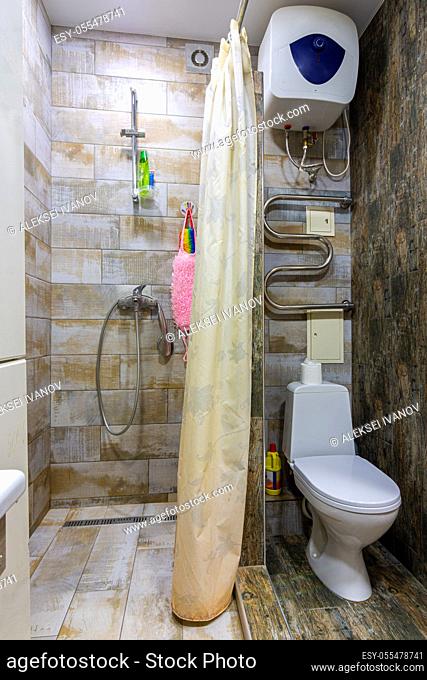 Small compact bathroom divided with shower curtain and toilet