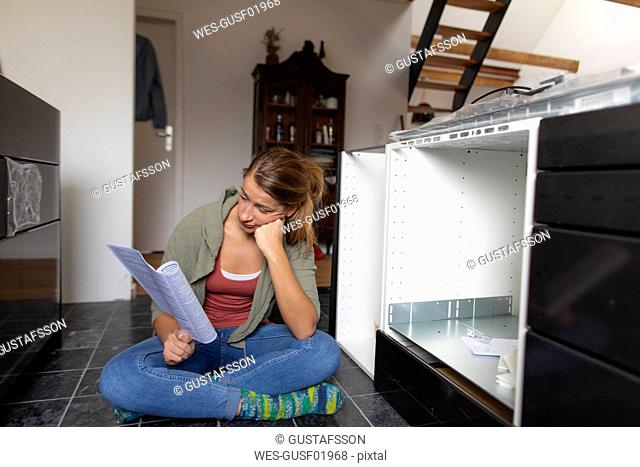 Frustrated young woman reading assembly instructions in kitchen