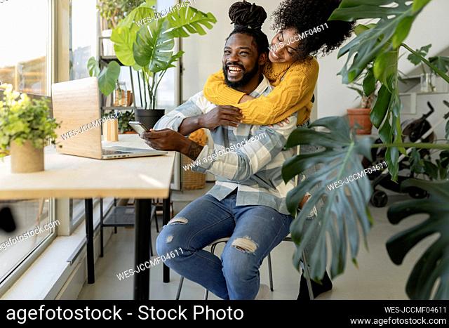 Young woman embracing boyfriend laughing in front of laptop at table