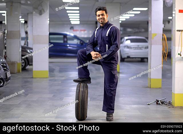 Portrait of smiling mechanic with a foot on a tyre in auto repair shop