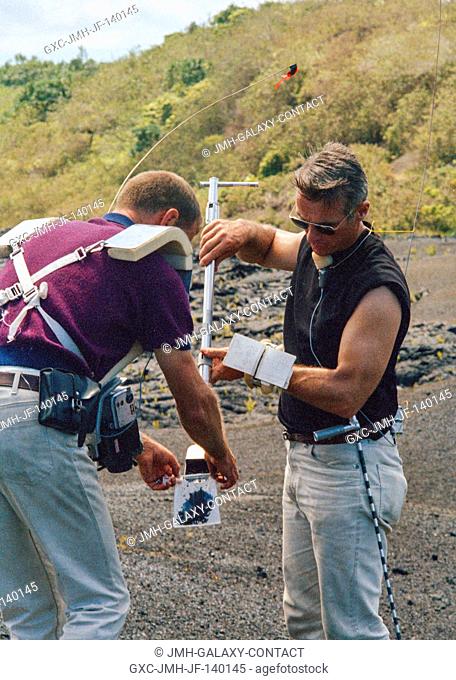 Astronaut Eugene A. Cernan (right), backup crew commander of the Apollo 14 lunar landing mission, pours a scoop-full of sample material into a bag held by...