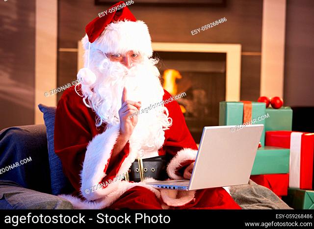 Modern Santa Claus sitting by fireplace using computer computer