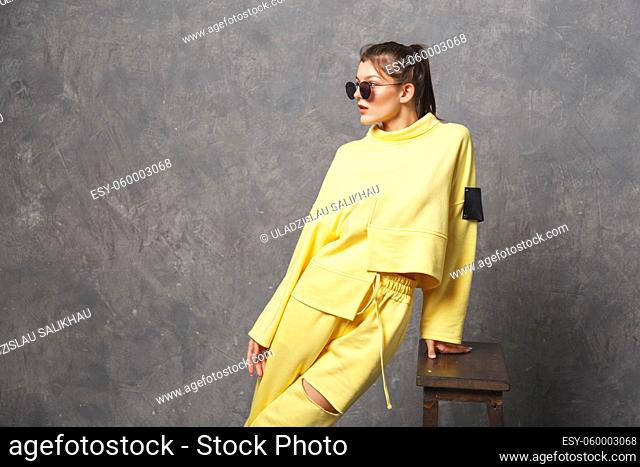 Young woman in yellow sportswear, pants and sweatshirt. Concept of fashionable sport outfit, indoors photo. Copy space