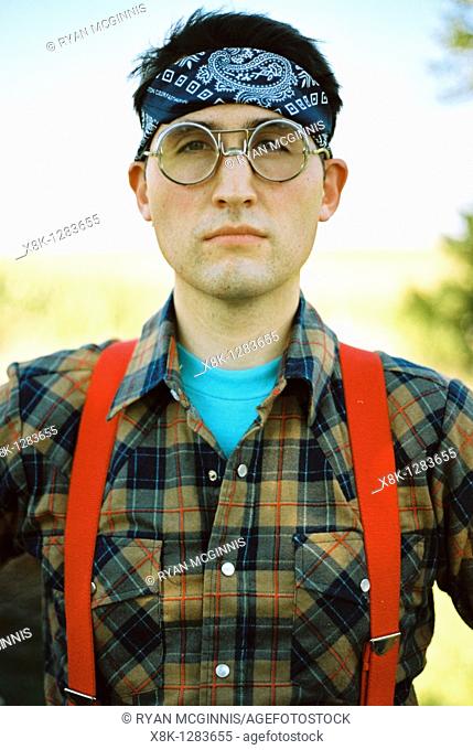A man wearing bomber glasses, a bandana, flannel, and suspenders