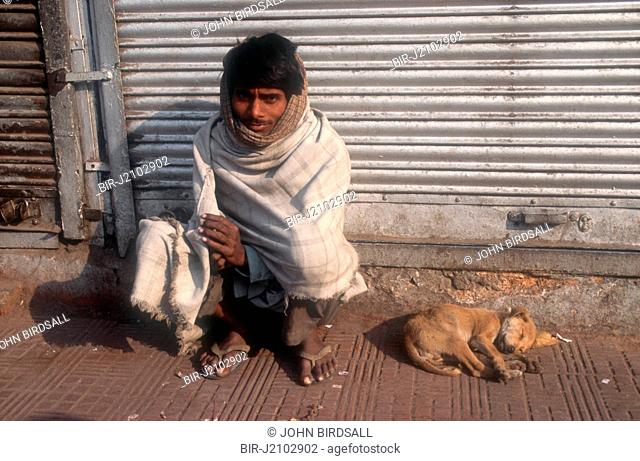Man sitting by side of road with puppy asleep beside him, Punjab, India