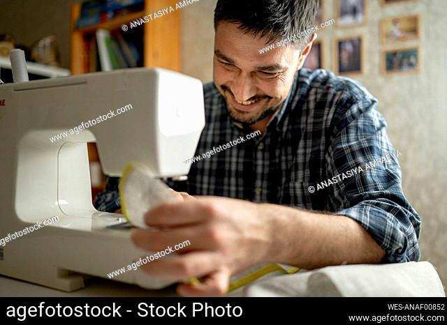 Smiling man using sewing machine at home