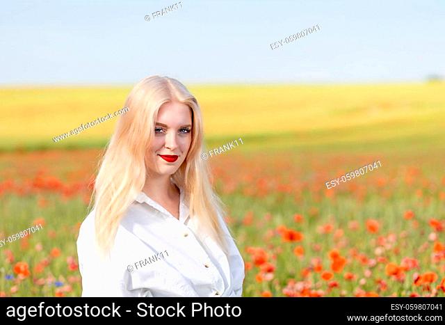 Smiling blonde girl is posing in red poppy field. Horizontally