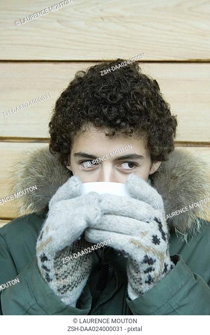 Teen boy in winter clothes drinking warm drink