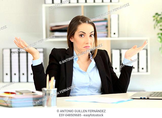 Front view portrait of a confused businesswoman shrugging shoulders looking at camera at office