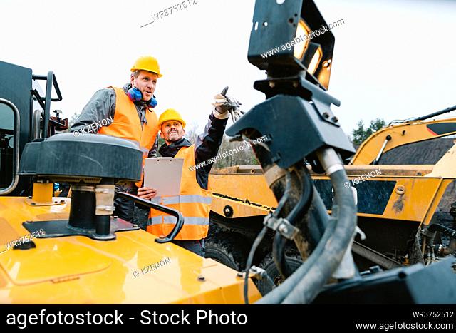 Two male workers on excavator in digging operation or quarry pictured on machinery