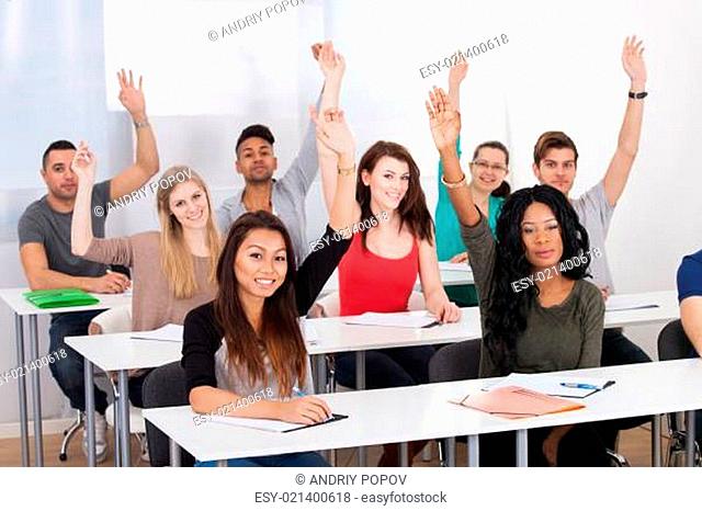 College Students Raising Hands In Classroom