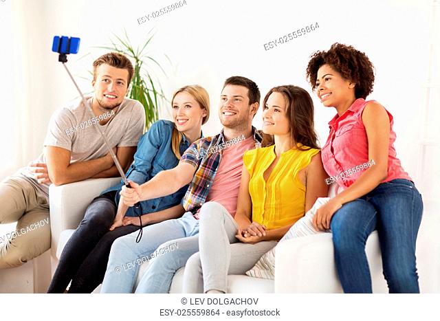 friendship, and people concept - group of happy friends taking picture with smartphone and selfie stick at home
