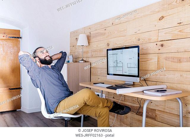 Smiling young man sitting at desk with floor plan on the computer