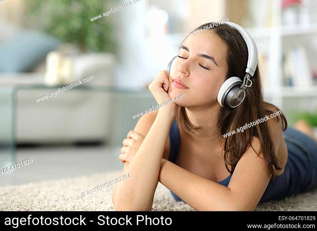 Relaxed woman listening music with headphone lying on the floor at home