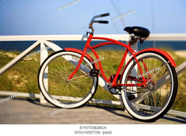 Red beach cruiser bicycle leaning against walkway rail on beach on Bald Head Island, North Carolina