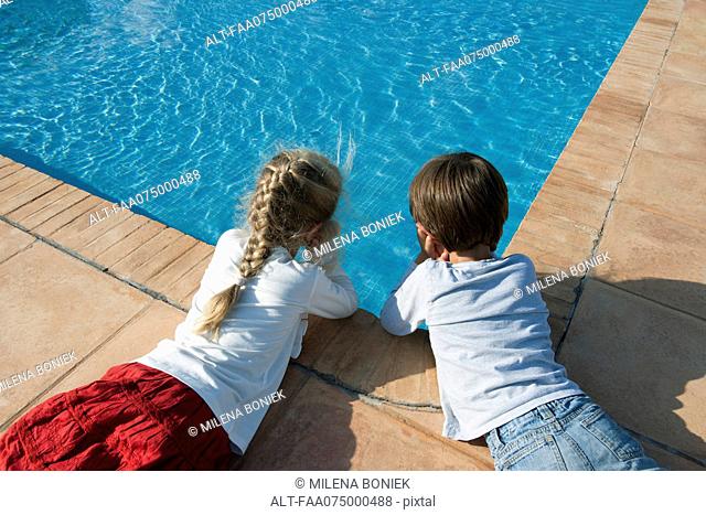 Children lying beside swimming pool, gazing at water