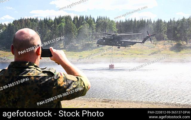 12 August 2022, Saxony-Anhalt, Elend: A Bundeswehr CH-53 helicopter takes water from the Mandelholz reservoir to fight a forest fire near Schierke