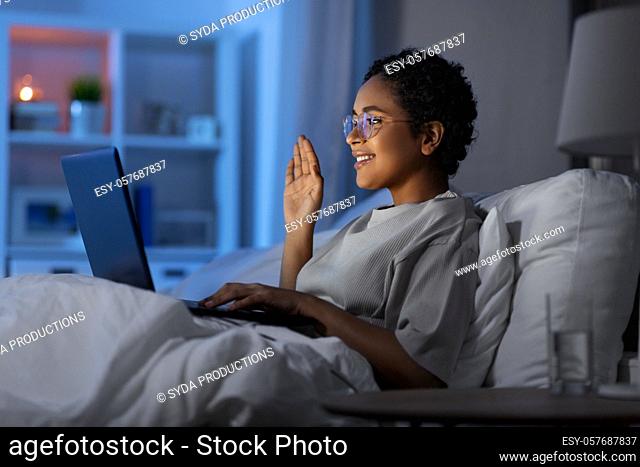 woman having video call on laptop in bed at night