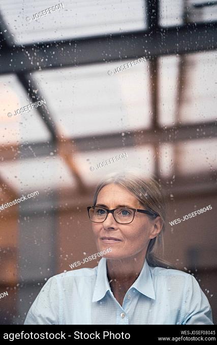 Thoughtful businesswoman seen through glass of work place