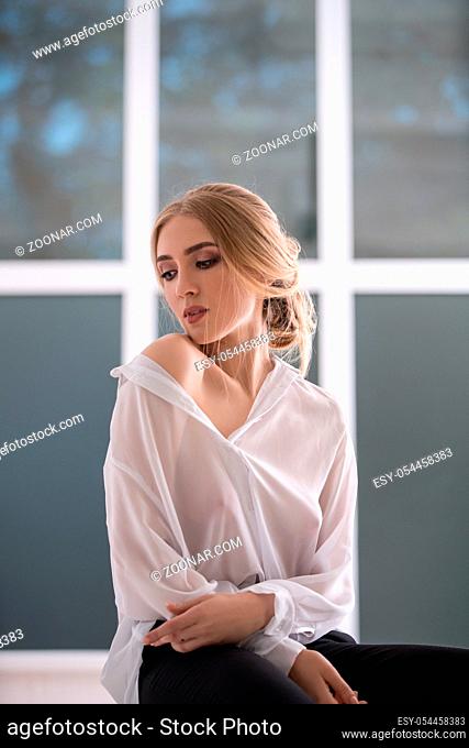Woman wearing sexy white shirt sitting on window sill studio portrait