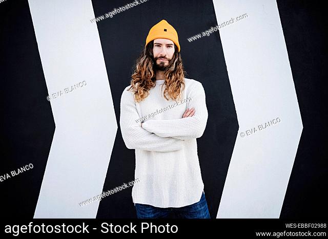 Hipster man with arms crossed standing in front of wall