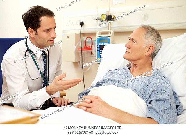 Doctor Sitting By Male Patient's Bed In Hospital