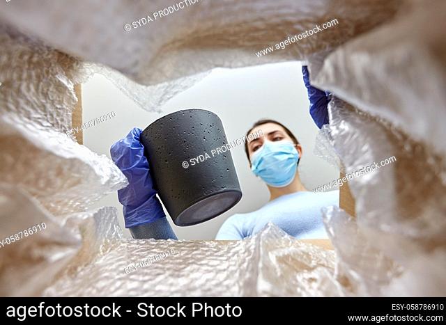 woman in mask opening parcel box with flower pot