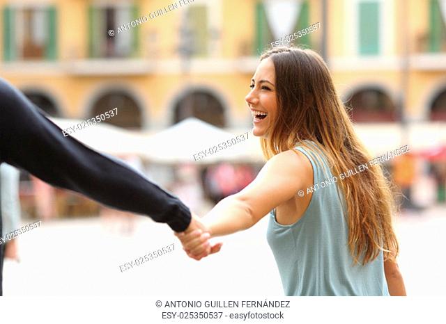 Happy tourist woman laughing and pulling her boyfriend in a touristic place