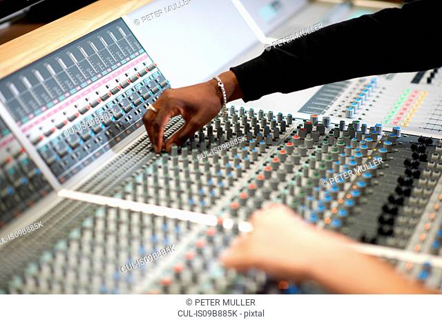 Hands of male college students at sound mixer in recording studio