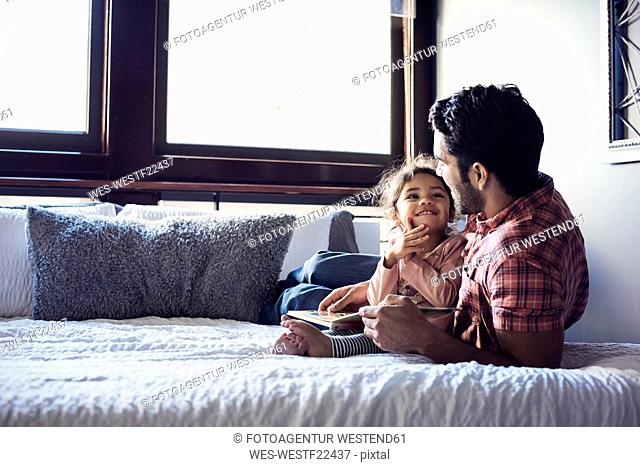 Father and daughter reading book, lying on bed