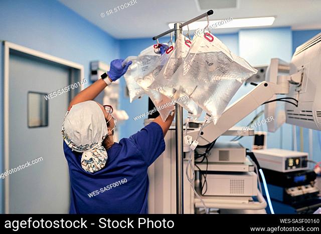 Male doctor removing IV drip bag while standing by monitoring machine in operating room