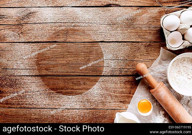 Christmas baking ingredients, kitchen utensils on old wooden background. Cooking dough, preparing egg yolk, flour, rolling pin, parchment paper, whisk, salt