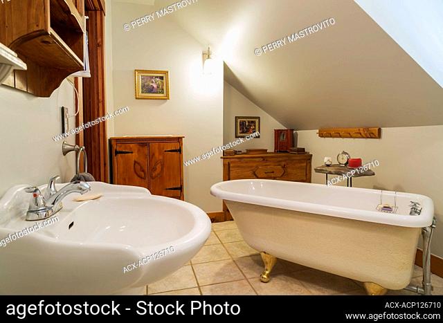 White pedestal wash sink, claw foot bathtub and antique pinewood cabinets in en suite with ceramic tiles on upstairs floor inside a 1990s contemporary Victorian...