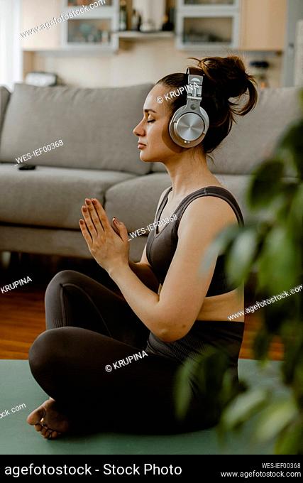 Woman with headphones meditating in living room