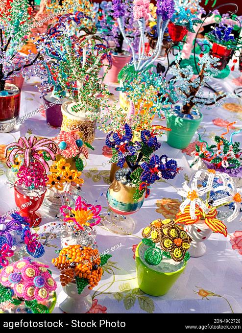 various decorative handmade artificial flowers in pots made of small plastic colorful beads sale in market fair