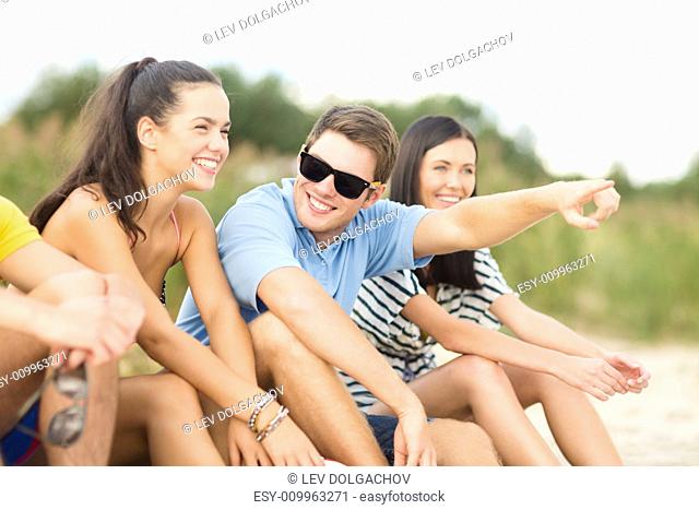 summer holidays, vacation, tourism, travel and people concept - group of happy friends sitting on beach and pointing finger