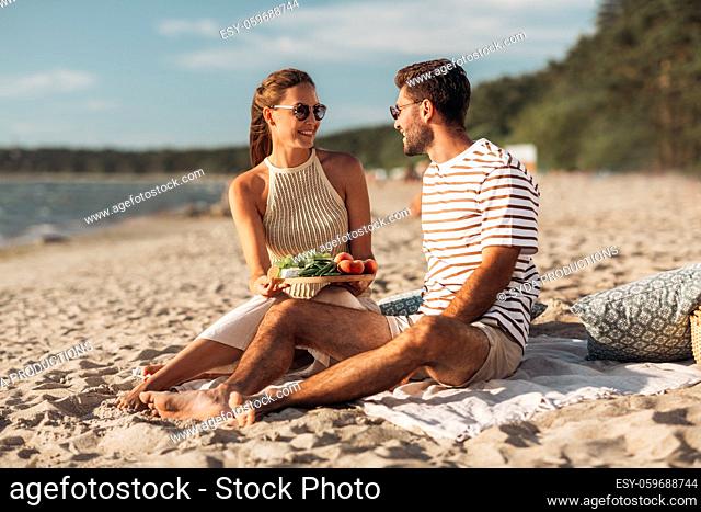 happy couple with food having picnic on beach