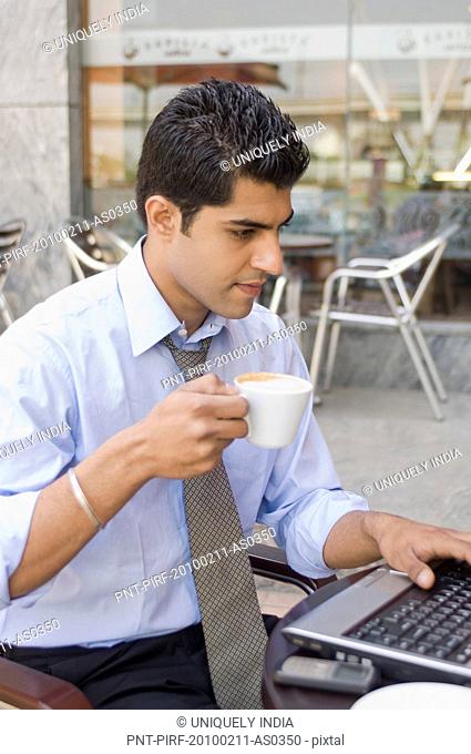 Businessman drinking coffee while using a laptop at a sidewalk cafe, Gurgaon, Haryana, India