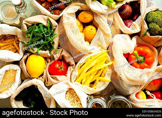 Fresh vegetables in eco cotton bags on table in the kitchen. Food shopping from market, conscious consumption, ban plastic