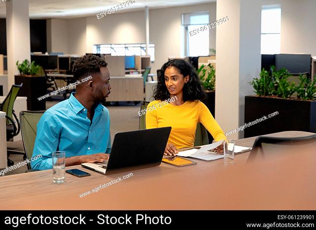 Confident male and female biracial business colleagues discussing while planning together at desk