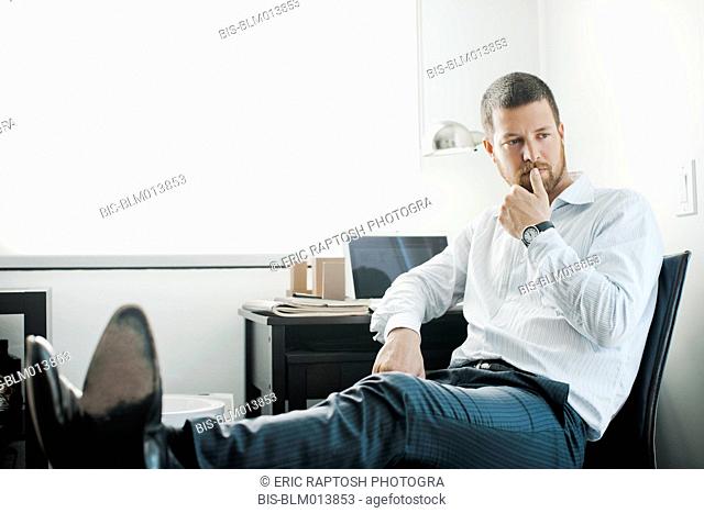 Hombre de negocios caucásico sentado en el escritorio con los pies en alto