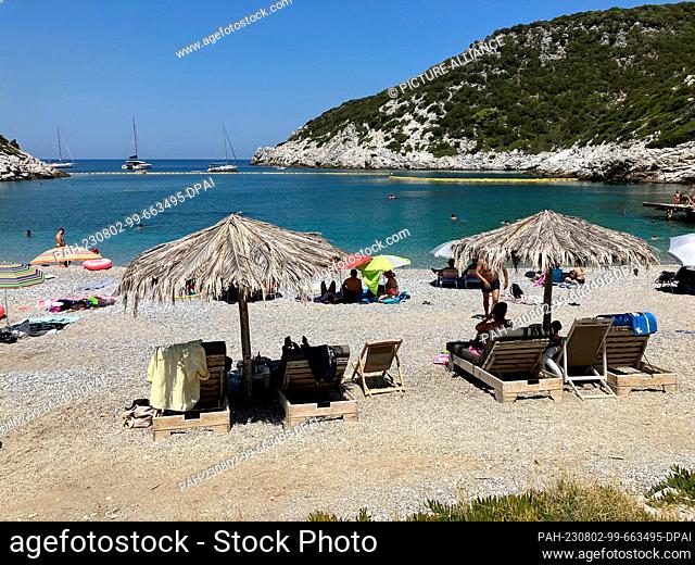 02 August 2023, Greece, -: People spend the hot summer day on a beach on the Sporades island of Skopelos. Some sit under their own colorful umbrellas