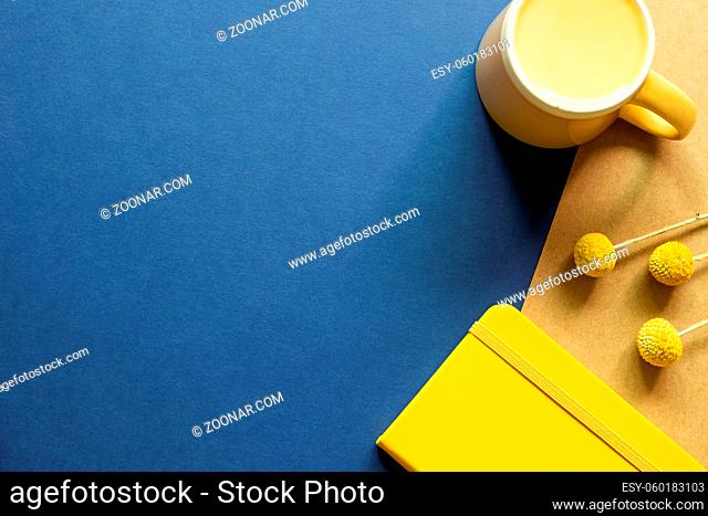 Yellow Notebook, mug cup, dry flowers on blue and brown background. flat lay, top view, copy space. Work and study place