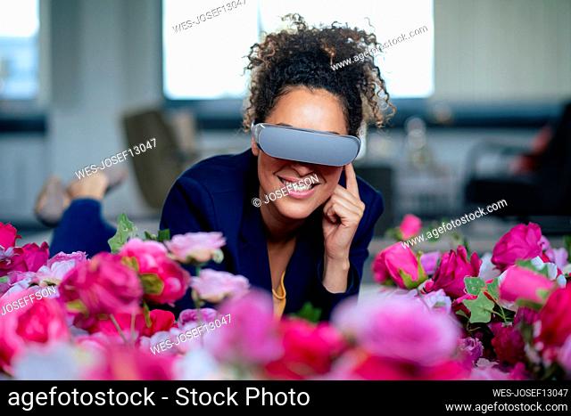 Smiling businesswoman using VR glasses by flowers at office