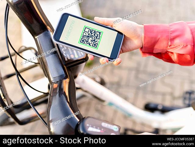 Woman scanning QR code through smart phone on electric bicycle