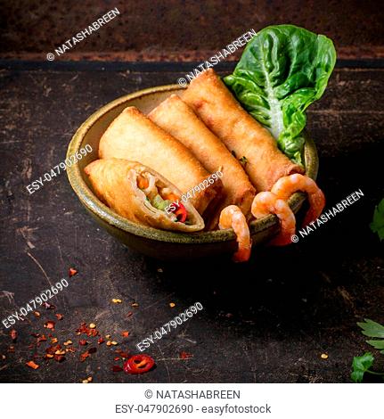 Fried spring rolls with vegetables and shrimps, served in ceramic bowl over black background. Square image with selective focus